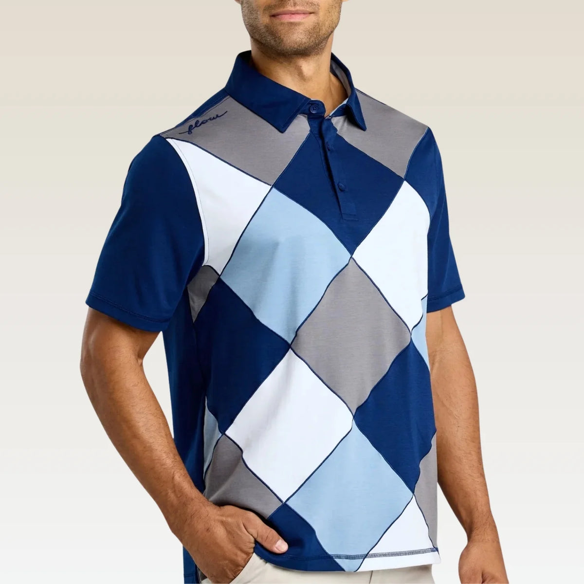 A man wearing a short-sleeve polo shirt with a geometric argyle pattern in navy blue, light blue, gray, and white, set against a plain light beige background.